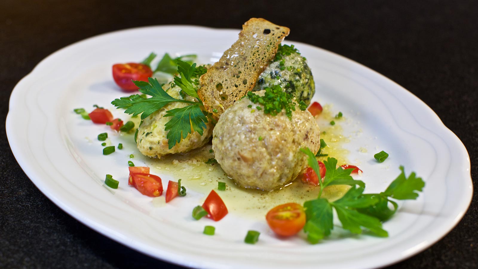 Dettaglio di un piatto di canederli decorati con pane e pomodorini