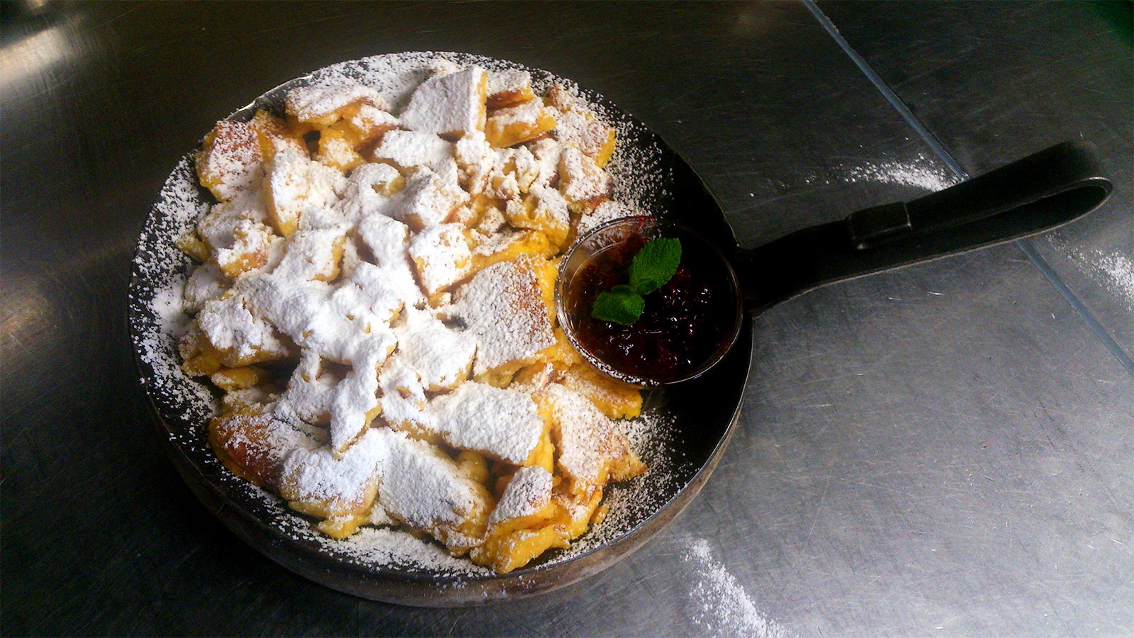 Tiroler Kaiserschmarren serviert mit Puderzucker und Heidelbeermarmelade in einer Kupferpfanne